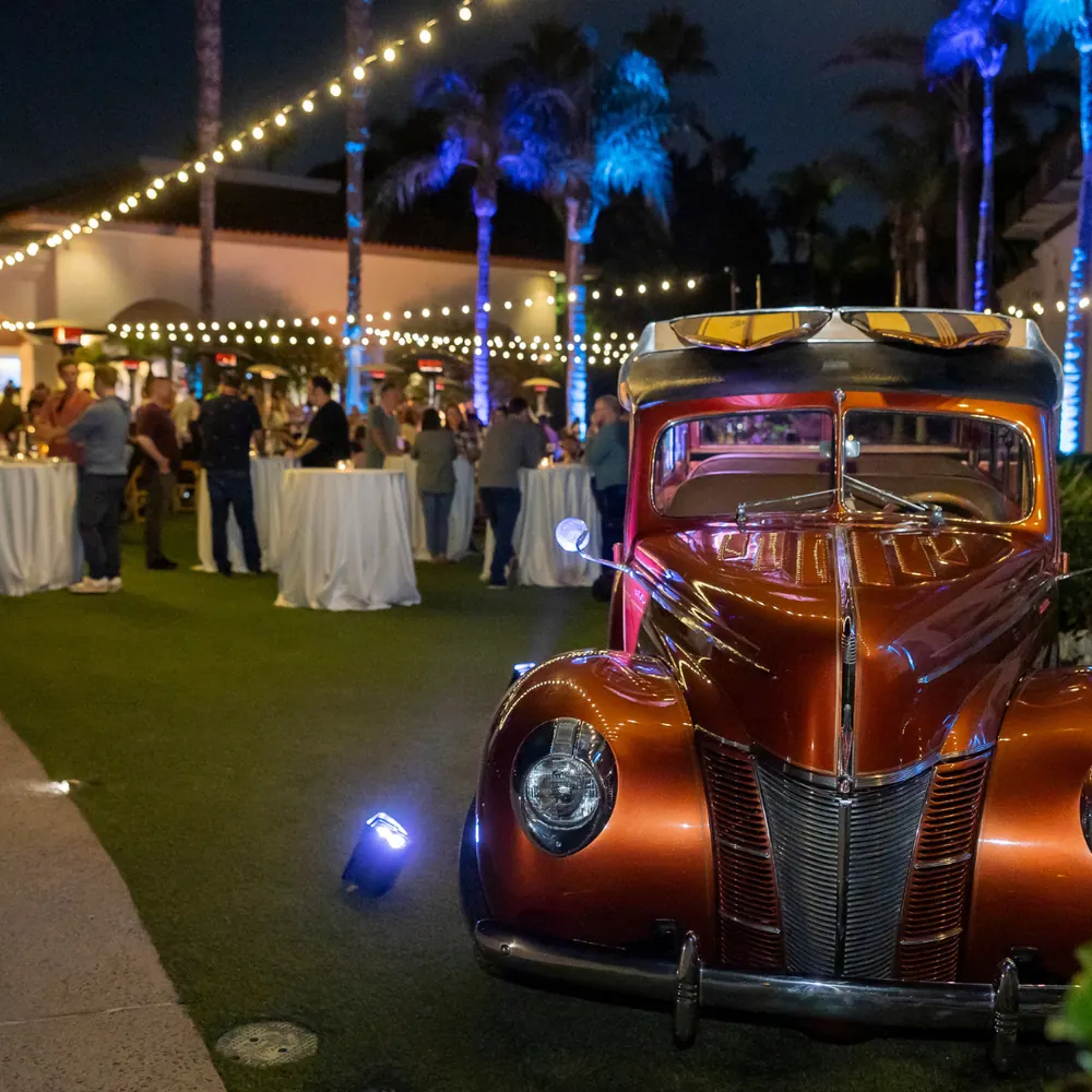 Coastal evening event in San Diego with vintage woody car, palm trees, and string lights