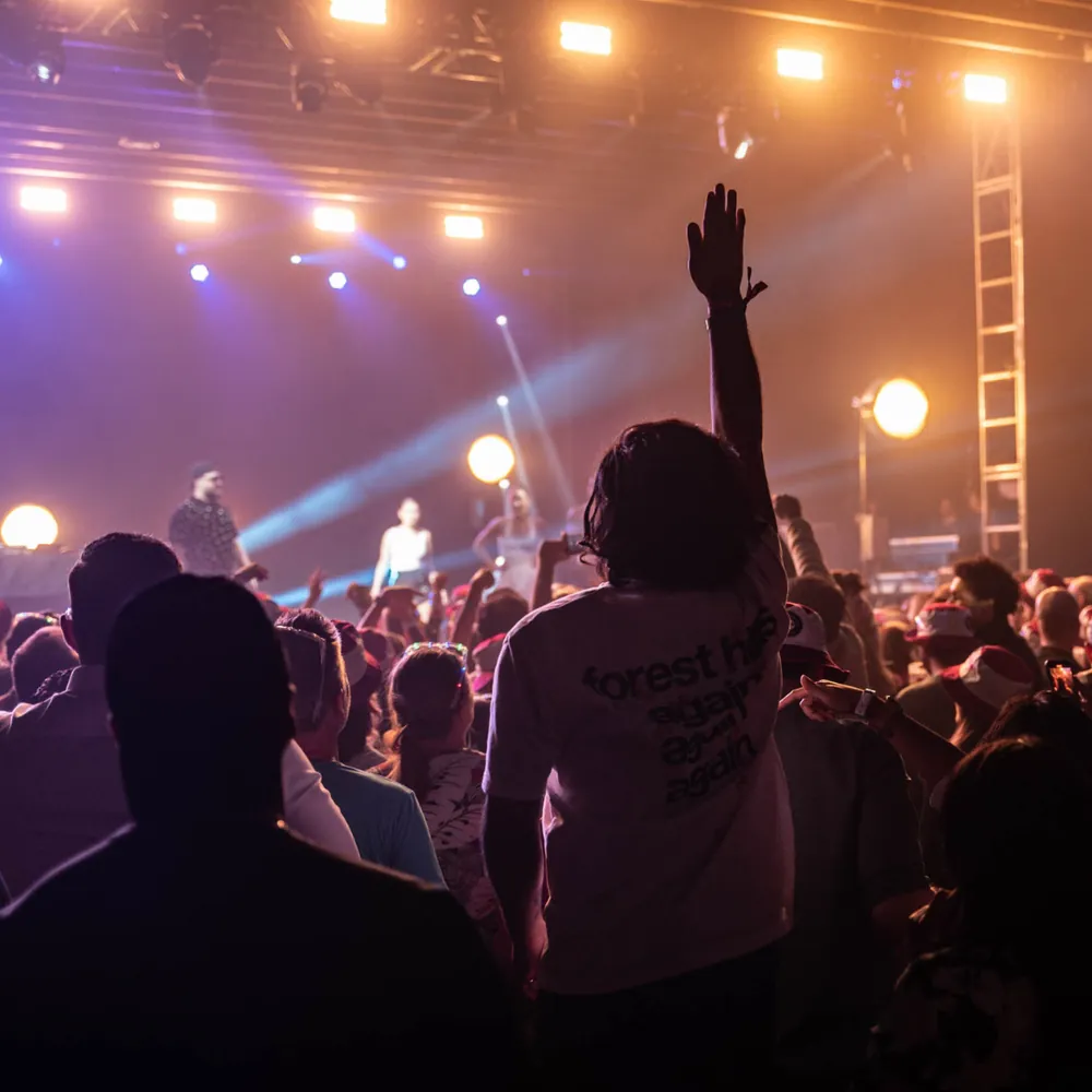 Macklemore concert audience with hands raised, stage lights overhead